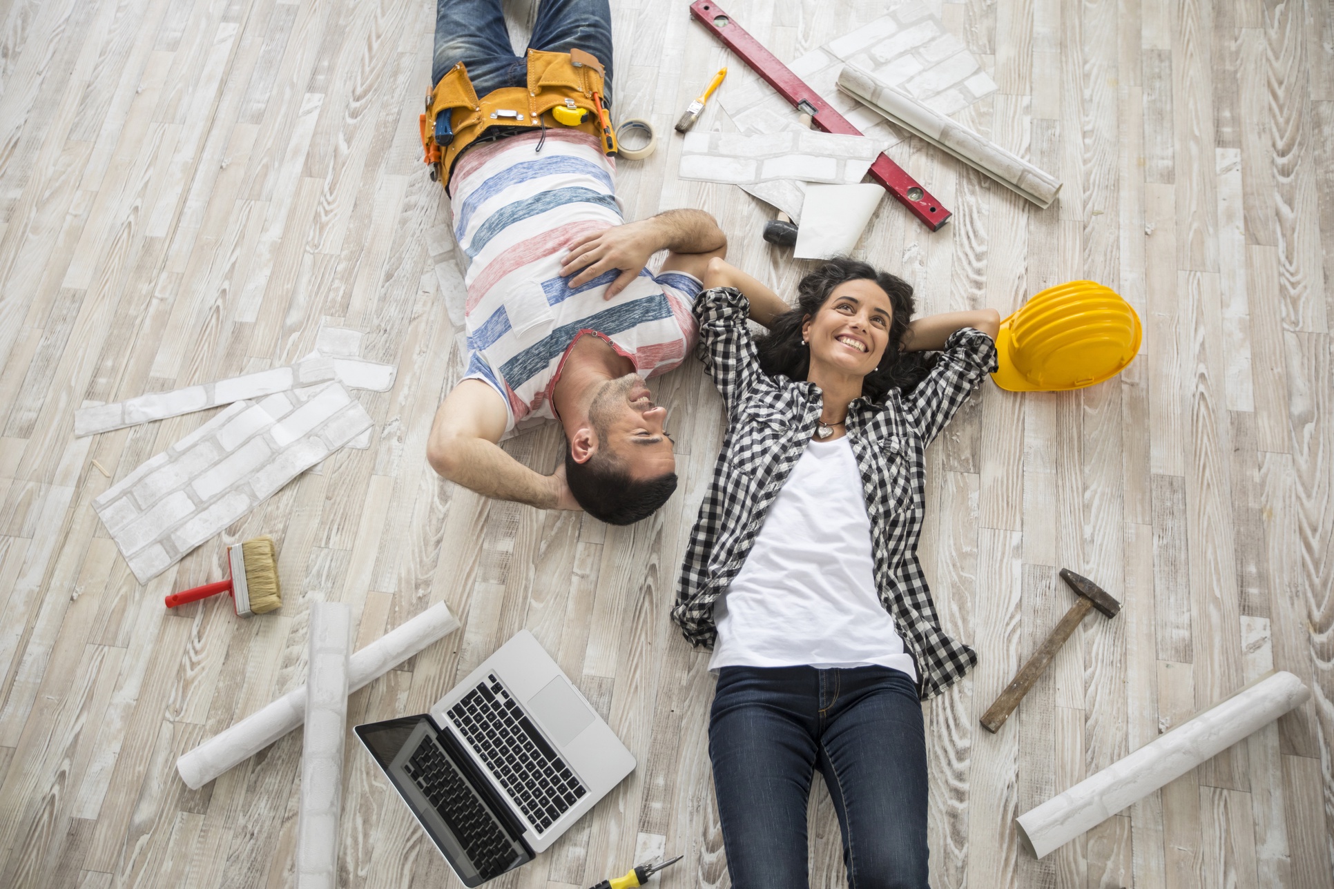 a happy couple lying on the floor with home construction tools