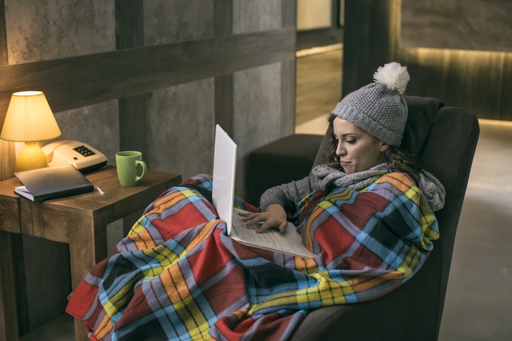 Girl with blanket wrapped around her while using a laptop at home